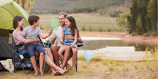 Mutter, Vater und ihre Kinder sitzen vor einem Zelt. Im Hintergrund ist Wasser zu sehen. 