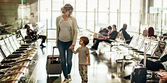 Eine schwangere Frau hält an ihren einen Hand ein Kind und der anderen Hand einen Koffer fest. 