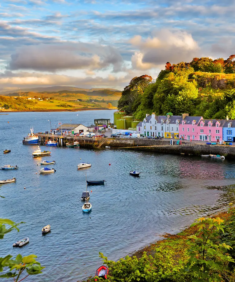 Man sieht eine kleine Stadt auf der Isle of Skye. Die Häuser sind bunt und stehen in einer Bucht am Wasser. 