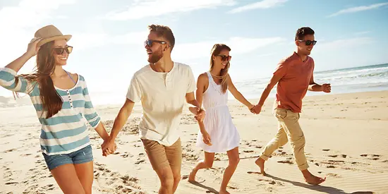 Zwei Pärchen gehen am Strand spazieren und halten Händchen. 