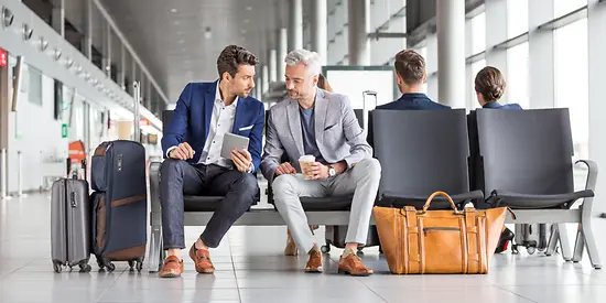 Zwei Männer sitzen am Flughafen und besprechen sich.