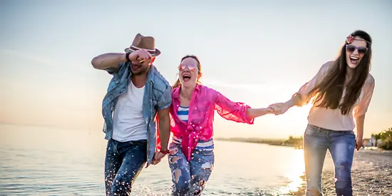 Drei Freunde gehen am Wasser spazieren und tragen alle eine Sonnenbrille.